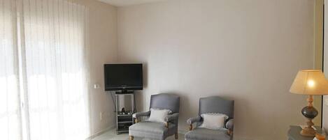 A hotel room with a bed, two armchairs, a TV, a lamp, and a window with curtains.