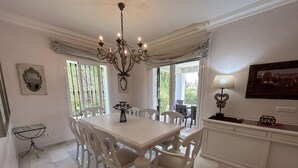 A dining room with a chandelier, white chairs, a table, and a view through large windows. - Villa Maisa Luxury Marbella (Marbella)
