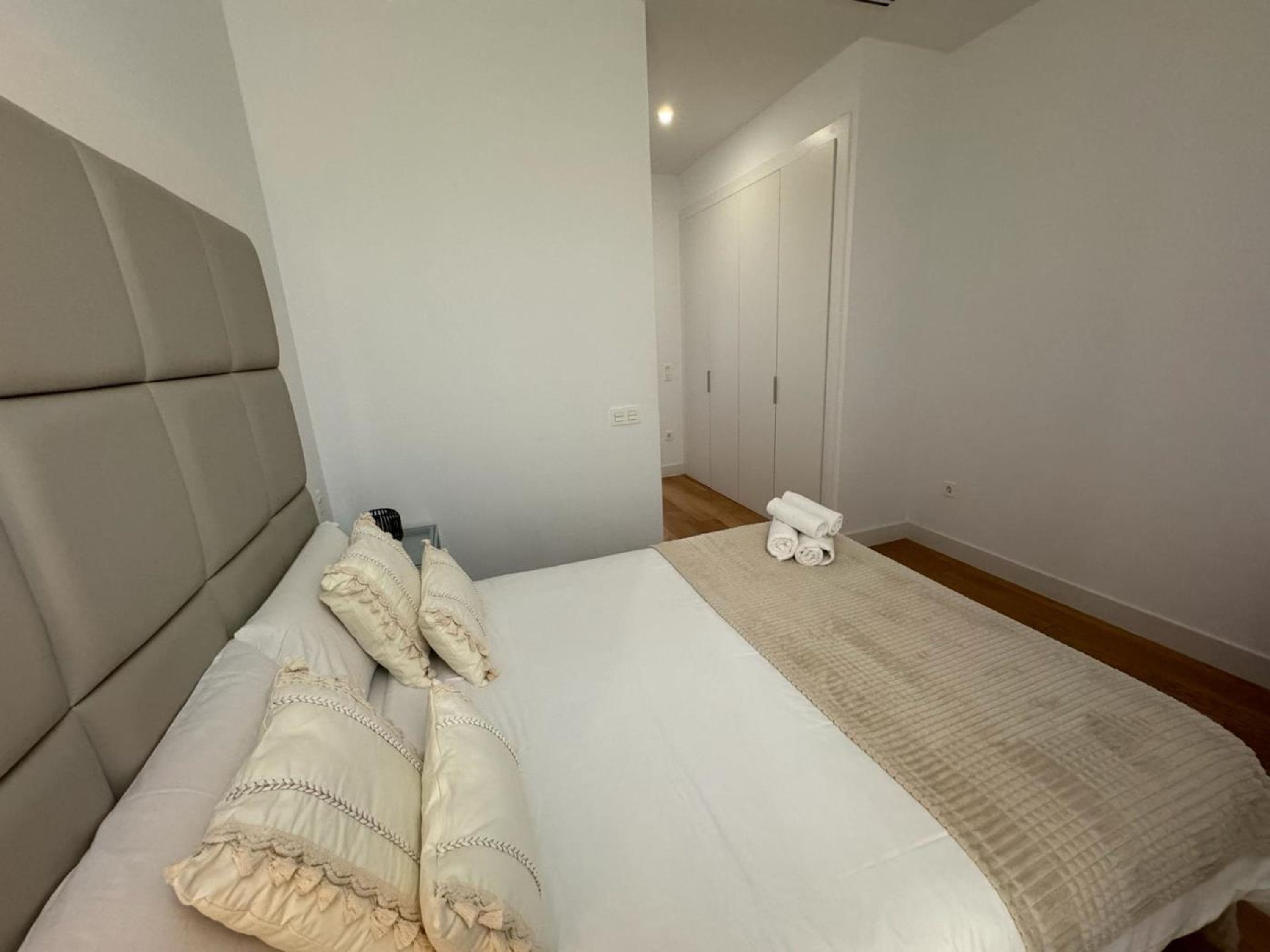 A neatly made bed with pillows and a blanket, a bedside table with a lamp, and a door leading to a closet.