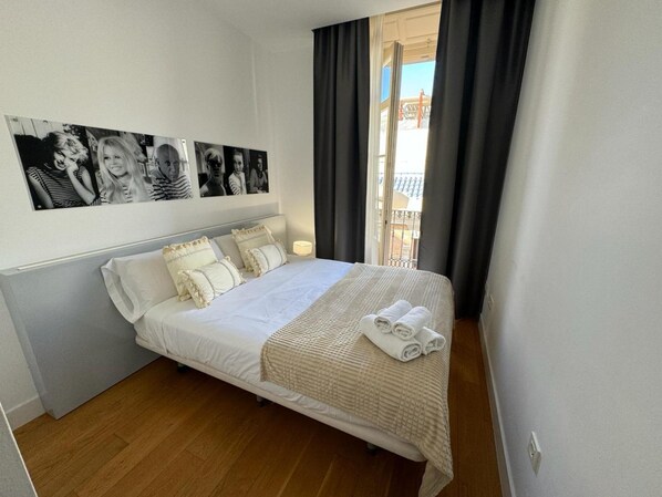 A neatly made bed with a white comforter and pillows, a small bedside table with a lamp, and a balcony with dark curtains. - Premium and Cathedral View 2 (Málaga)
