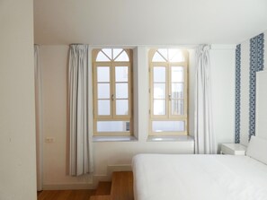 A bedroom with a bed, two windows with curtains, a wooden floor, and a patterned wall. - Premium and Cathedral View 1 (Málaga)