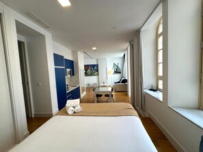 A modern hotel room with a large bed, a small kitchenette, a dining area, and a view of the sea through a window. - Premium and Cathedral View 1 (Málaga)