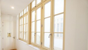Un pasillo con ventanas amplias, piso de madera y una puerta con placa.