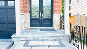Une maison à deux étages, construite en briques, avec une porte d’entrée sombre et un porche abrité.