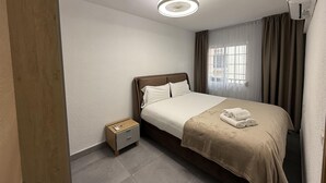 A hotel room with a bed, a nightstand, a ceiling light, a window with curtains, and an air conditioning unit.