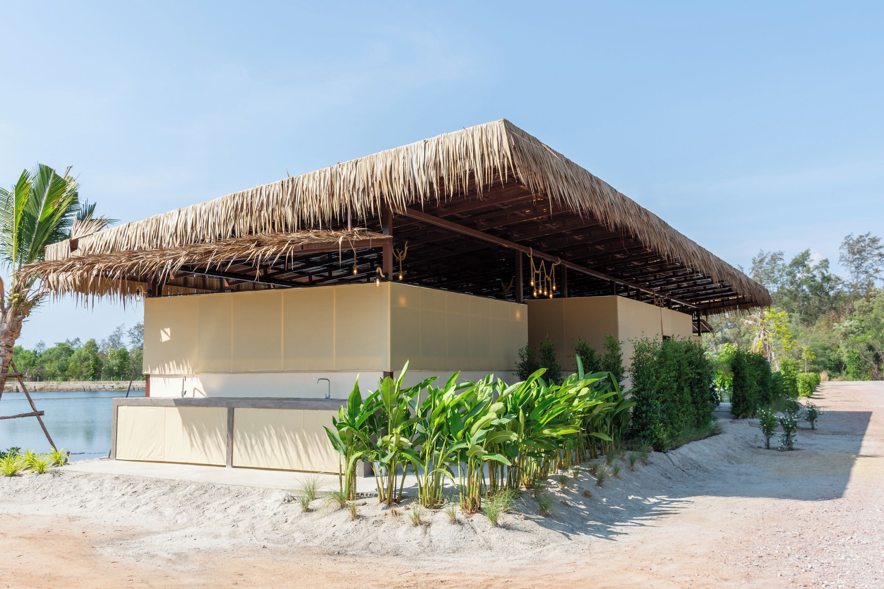 Una estructura frente al mar con techo de paja, un primer plano arenoso y vista despejada del agua.