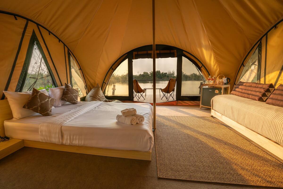 A tented accommodation with two beds, a small table, and chairs by a window overlooking a body of water.