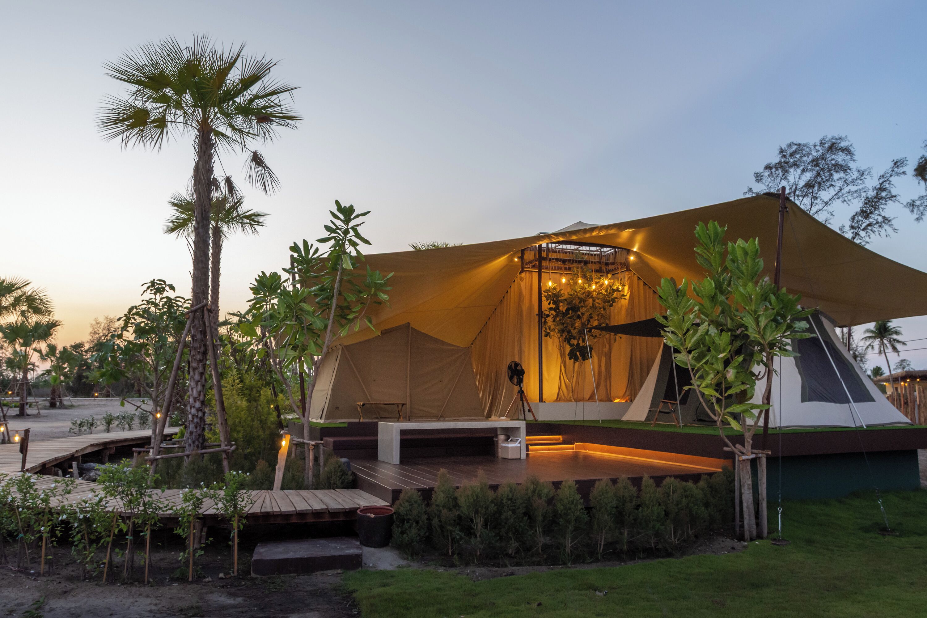 A large tent with a flat roof and a platform in front, surrounded by greenery and palm trees.