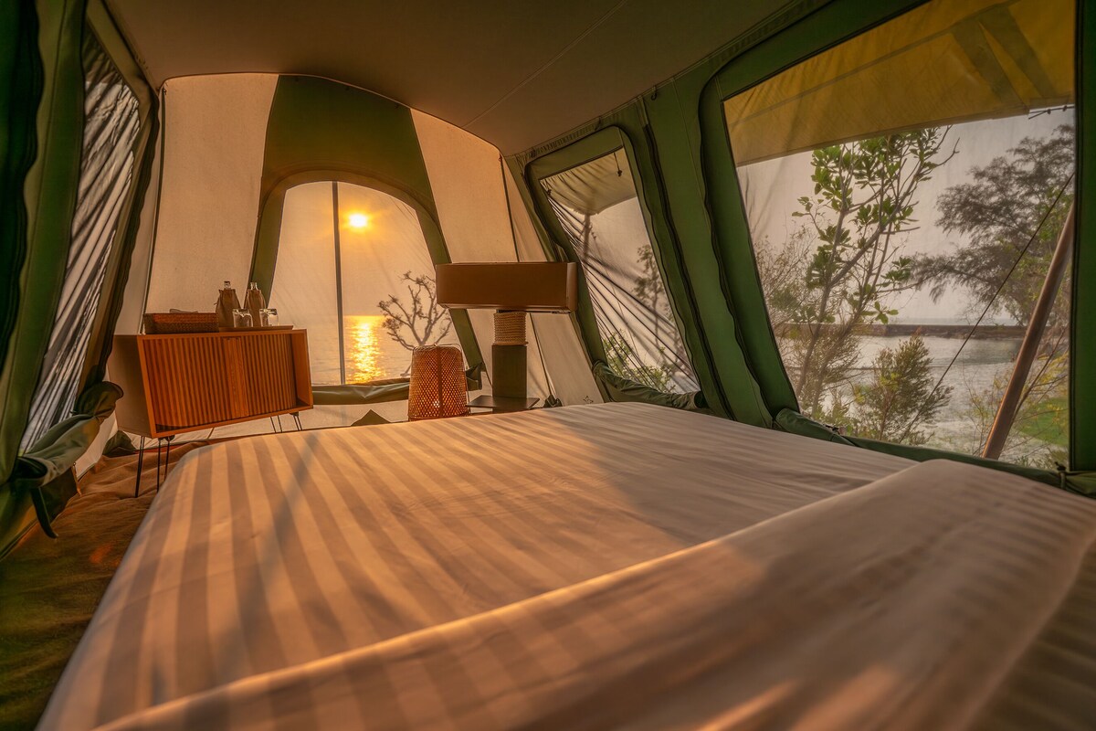 A tented room with a bed, a table, and a lamp.