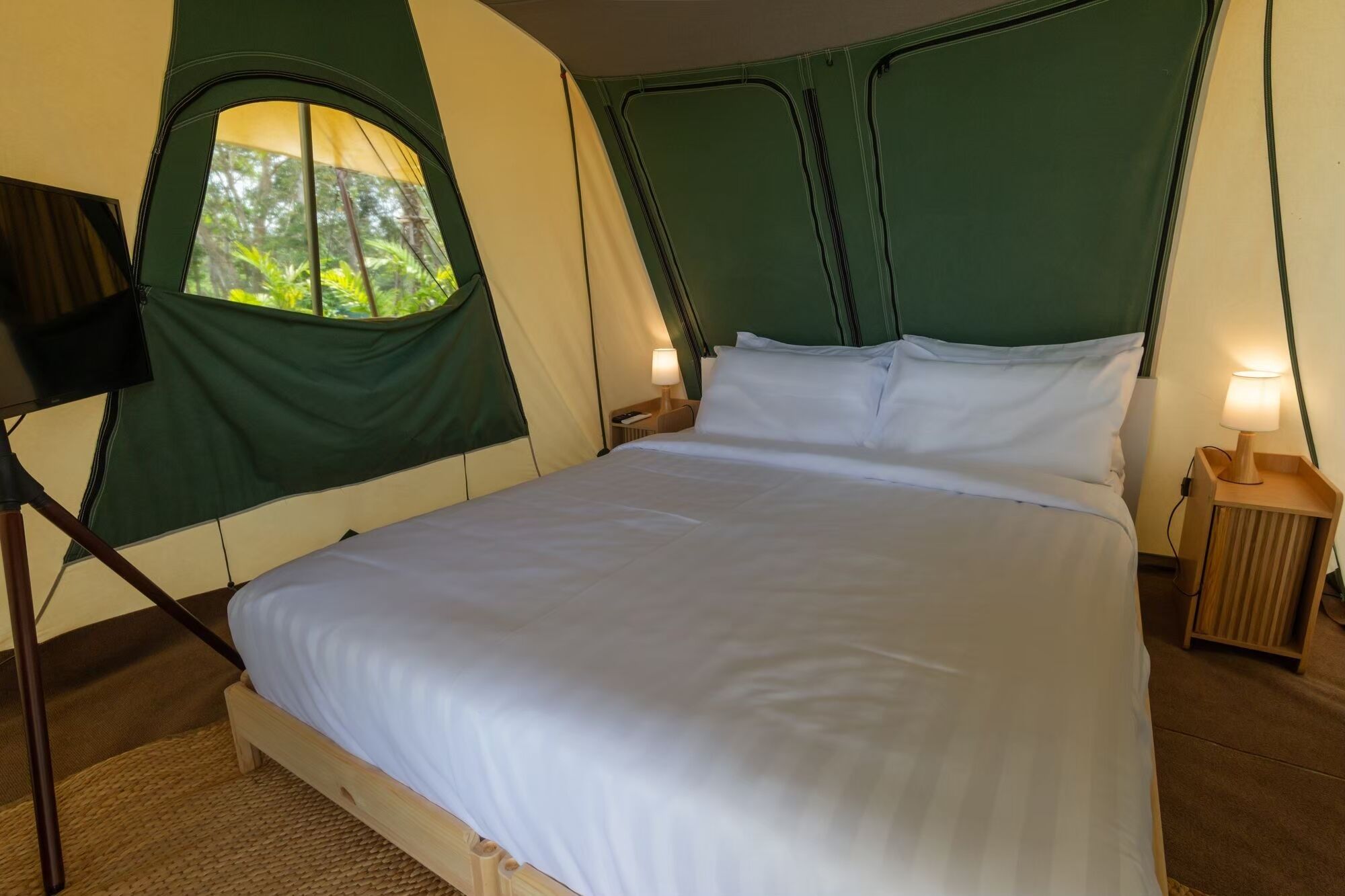 A bed with a green headboard and a window, a lamp on the side, and a wooden floor.