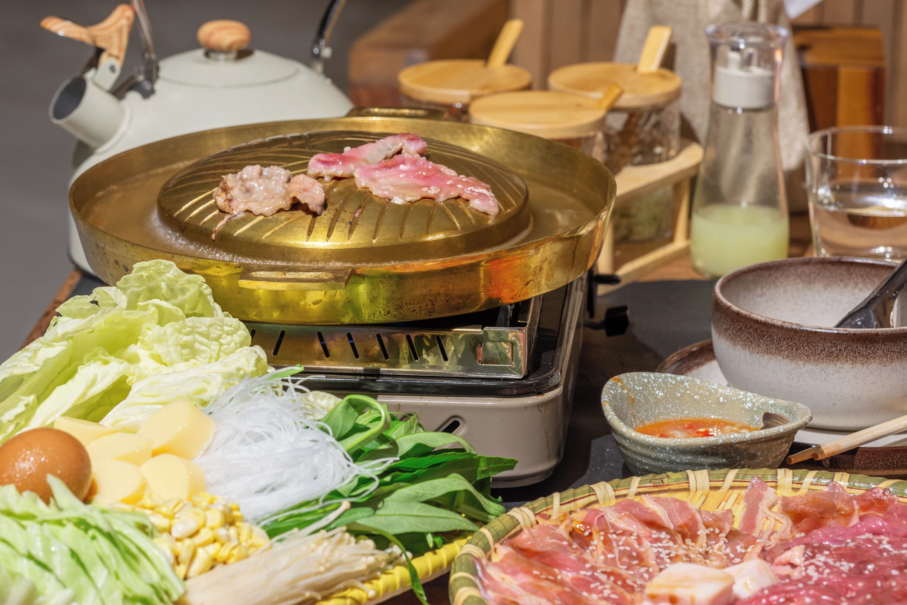 Une table où l’on prépare une fondue, avec divers ingrédients et une théière en arrière-plan.