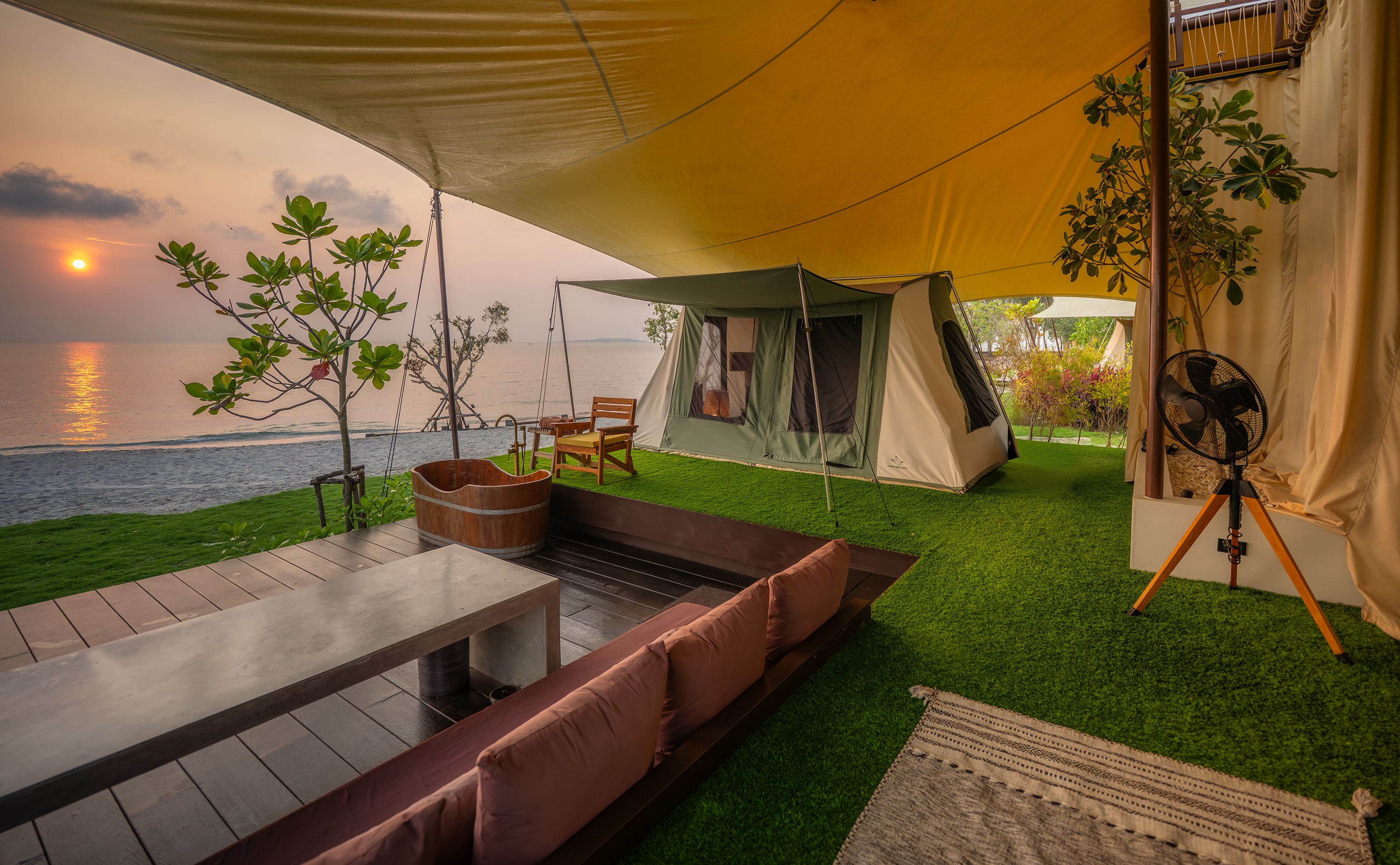 A tented outdoor area with a view of the sea, a wooden table, and a bench.