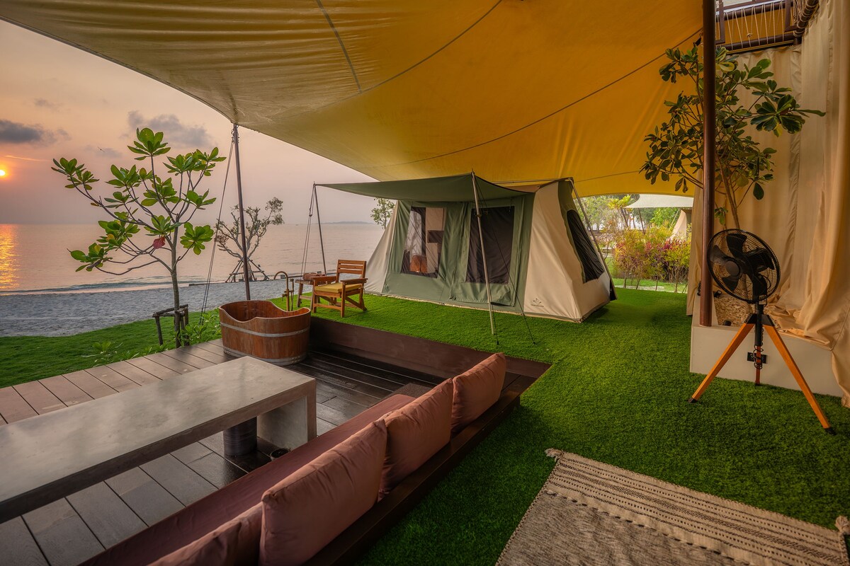 A tented outdoor area with a view of the sea, a wooden table, and a bench.