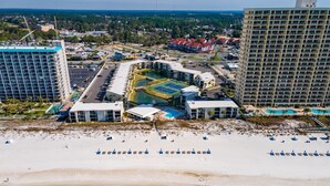 An aerial view of a resort with multiple buildings, a large pool, and a beach with sun loungers.