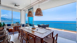 Un balcon spacieux offrant une vue sur l’océan, un coin repas avec des meubles en bois et de grandes fenêtres.