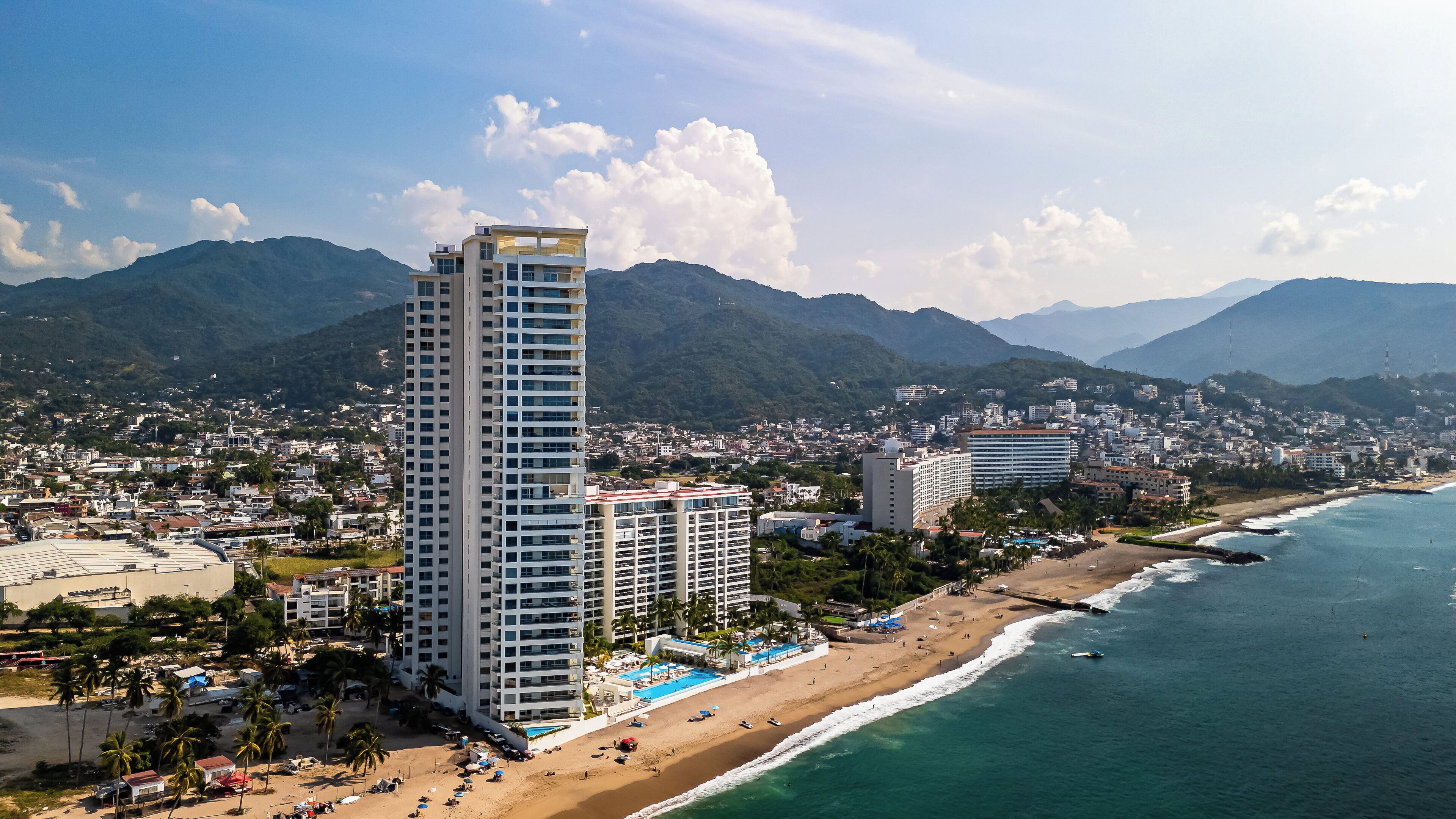 A high-rise hotel with multiple floors, a beachside location, and a view of the ocean and mountains in the background.