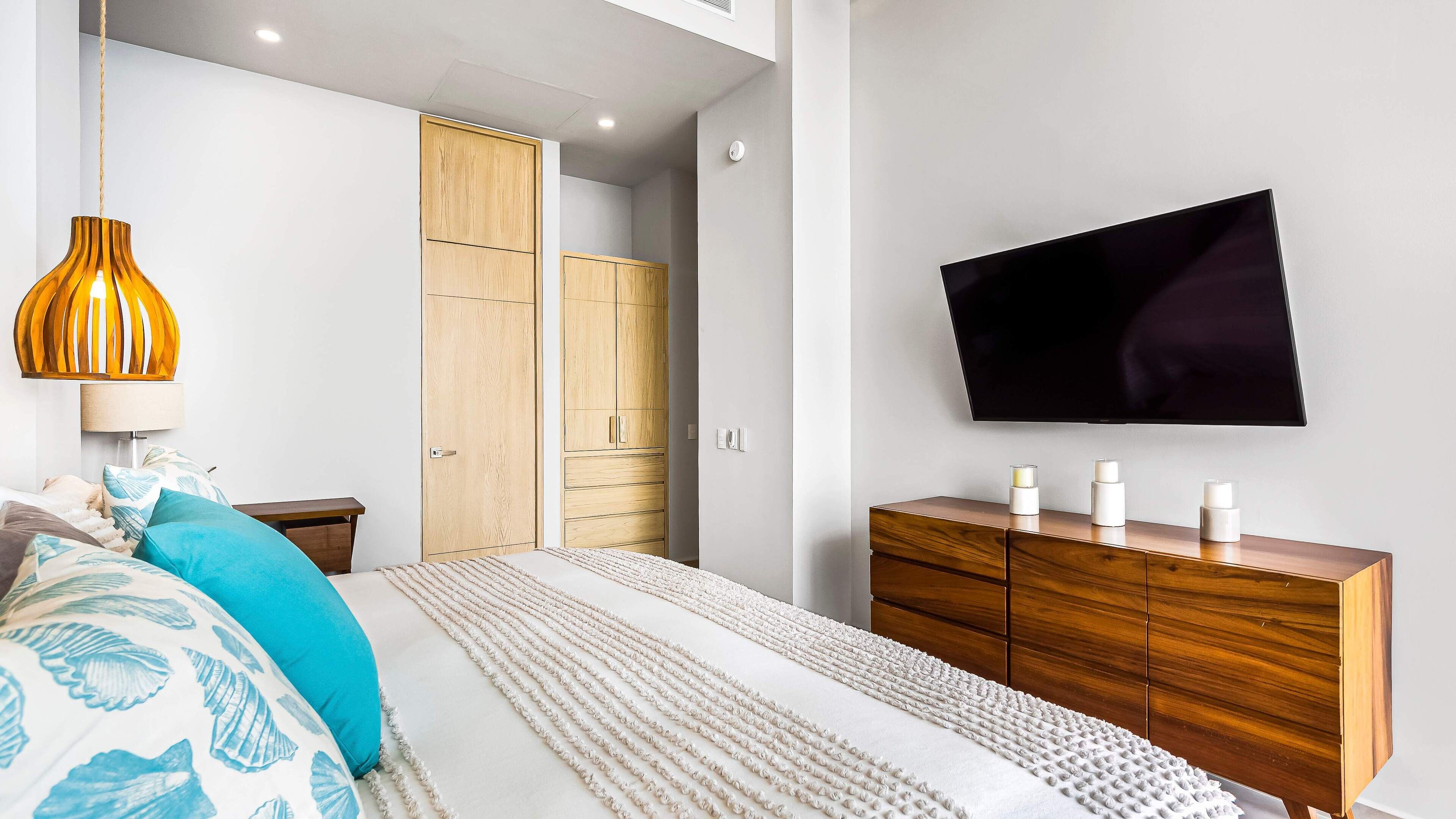 Un dormitorio con una cama, un armario de madera, un televisor y una lámpara colgante.