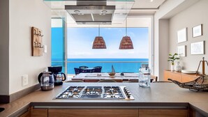 Une cuisine moderne équipée d’une cuisinière à gaz, d’une machine à café et offrant une vue sur l’océan.
