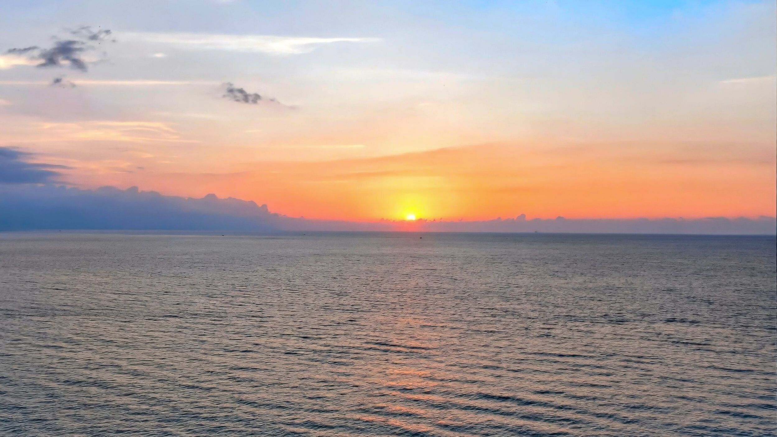 A sunset over a calm sea with a distant shoreline.