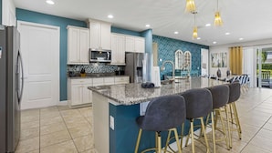 A modern kitchen with white cabinets, a granite countertop, and a central island with bar stools. - The Enchanted Collection: Burma Manor (Kissimmee)