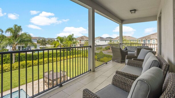 A covered balcony with outdoor furniture, a view of a residential area, and a swimming pool. - The Enchanted Collection: Burma Manor (Kissimmee)