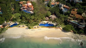 An aerial view of a resort with multiple swimming pools, a sandy beach, and lush greenery.