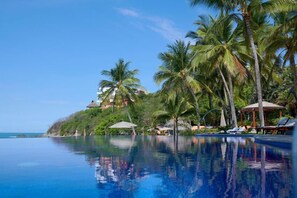 Piscina de un resort con palmeras y vistas a la playa.