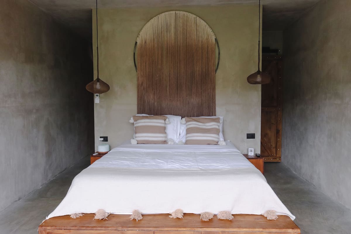 A bed with a white mattress and two pillows, a wooden headboard, and two pendant lights.