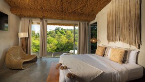 A bedroom with a large bed, a woven chair, and a view of greenery through the window. - Dar Lamia Boutique Hotel (Quepos)