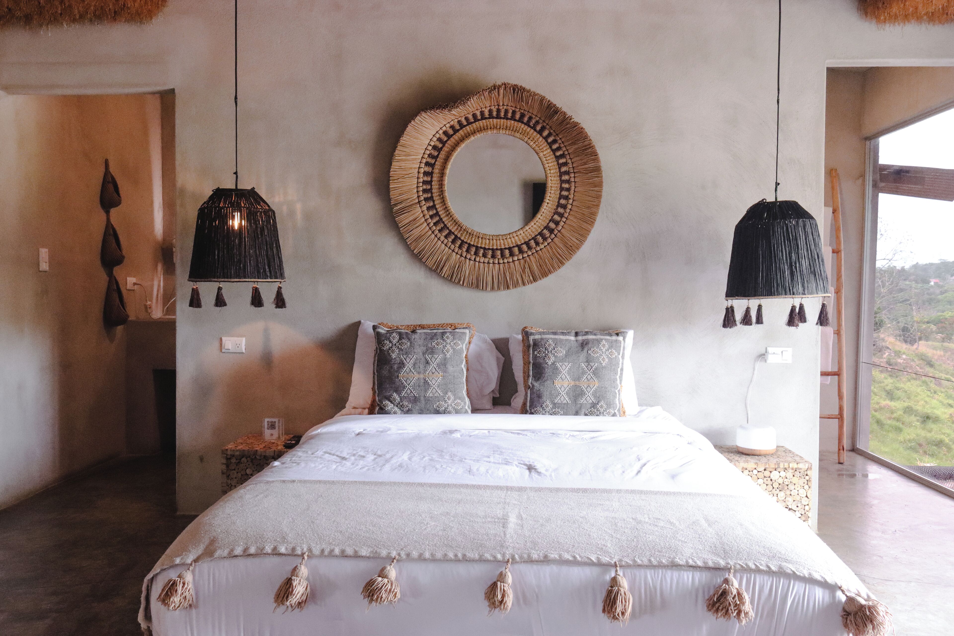 Un dormitorio con una cama grande, dos lámparas colgantes, un espejo redondo y vistas al exterior.