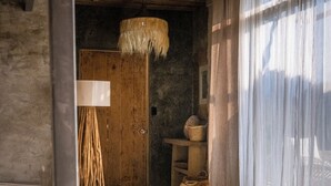 A rustic room with a straw hat on a bed, a wooden door, a lamp, and a window with sheer curtains. - Dar Lamia Boutique Hotel (Quepos)