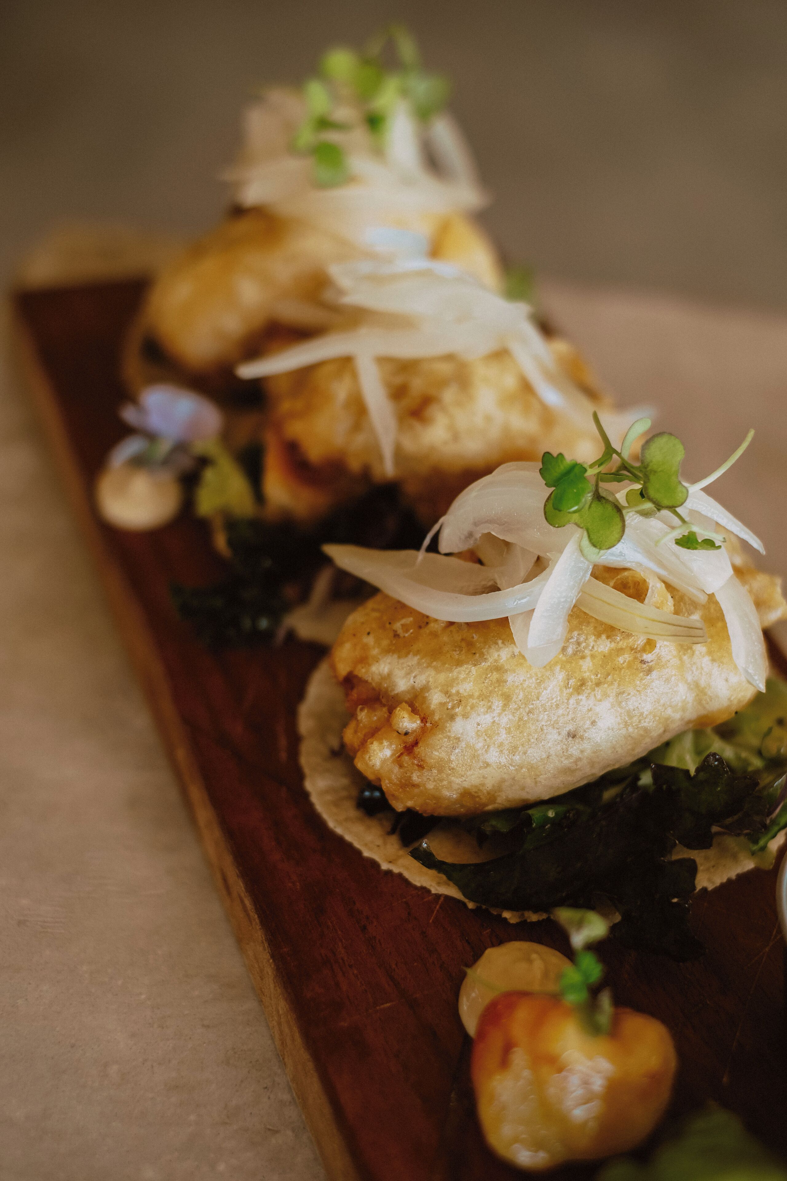 Une planche de service en bois sur laquelle sont disposées trois bouchées, chacune garnie d’une petite feuille verte et de rondelles d’oignon.