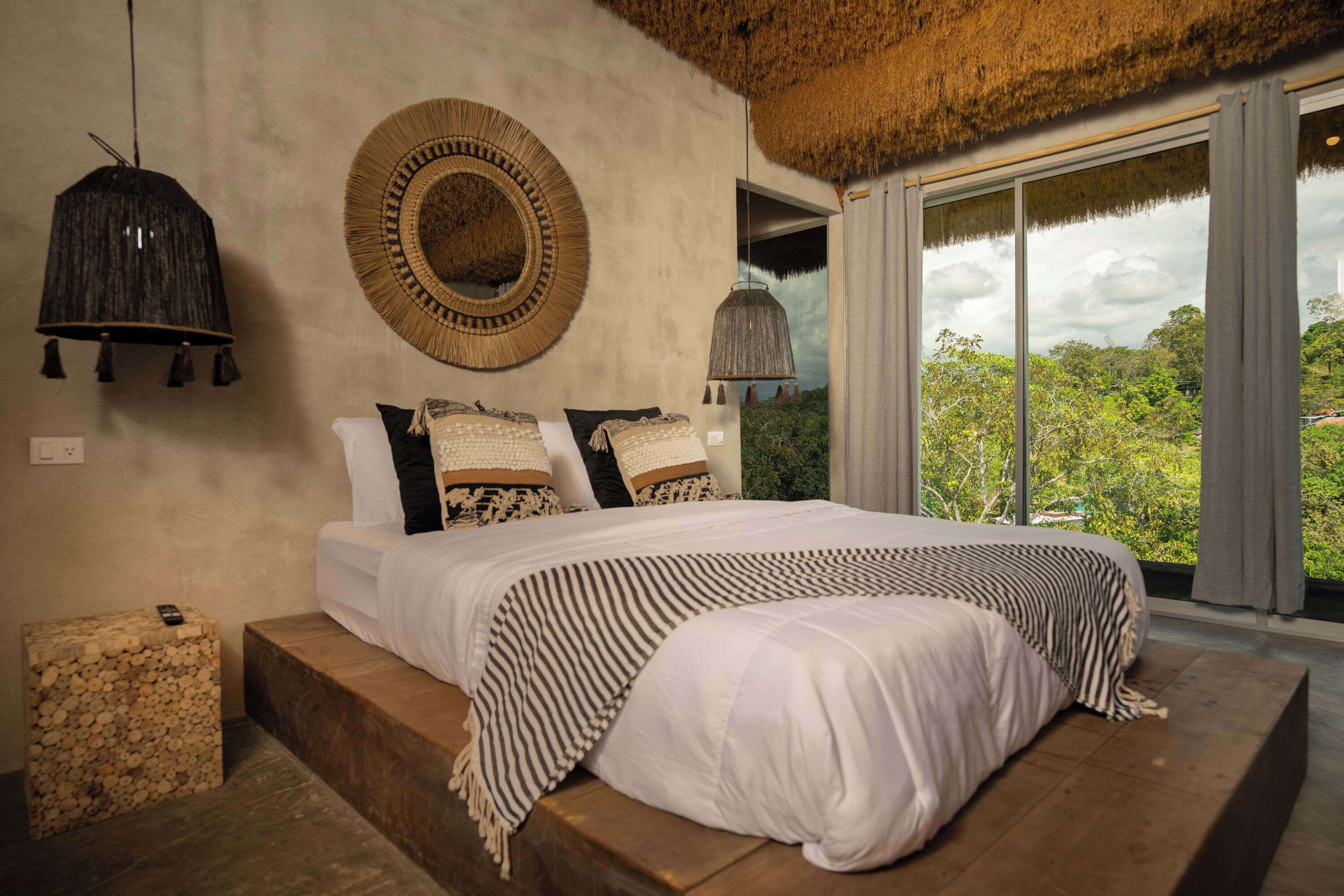 A bedroom with a large bed, a round mirror, and a hanging light fixture.