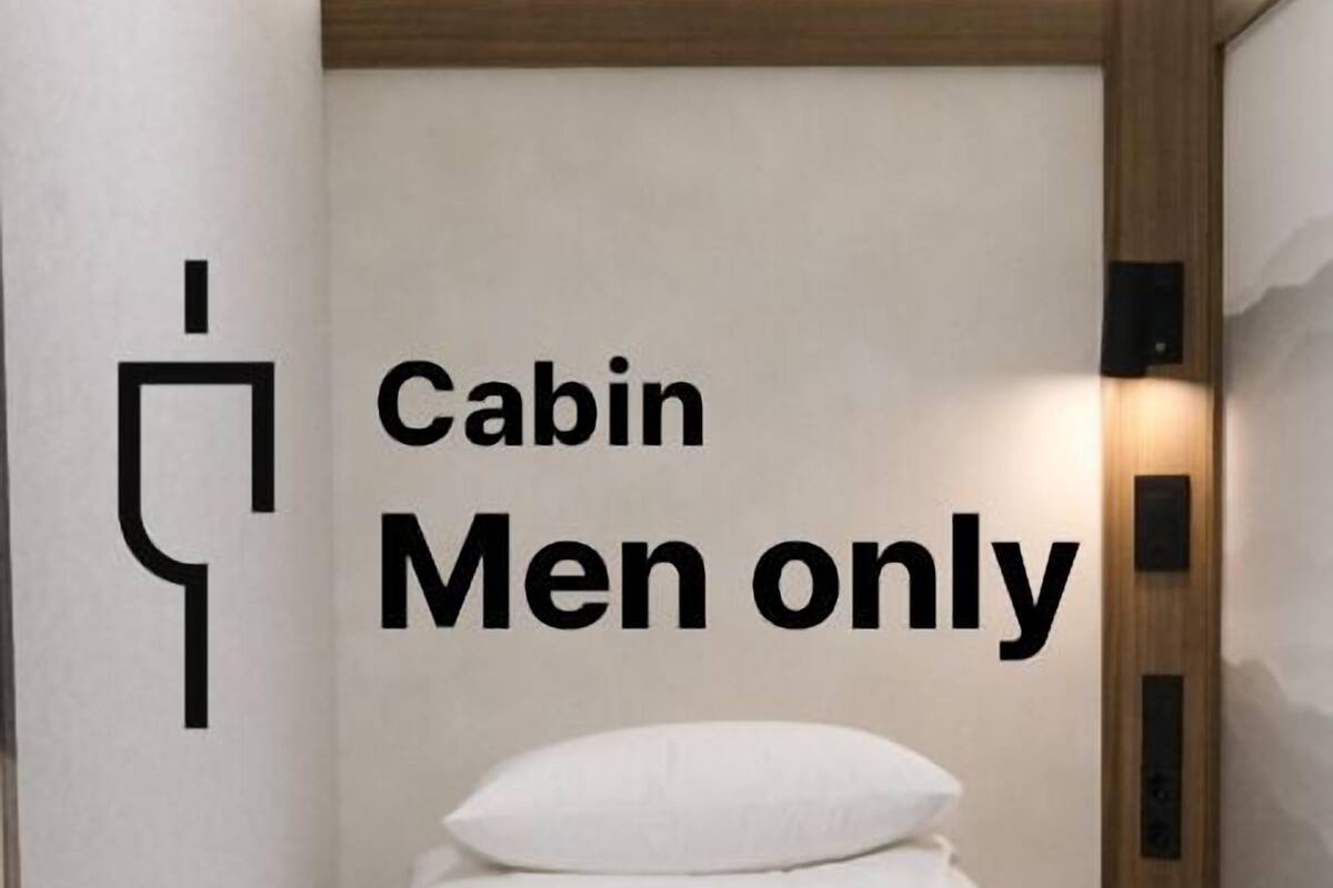 A cabin room with a bed, a wooden wardrobe, and a sign indicating it is for men only.