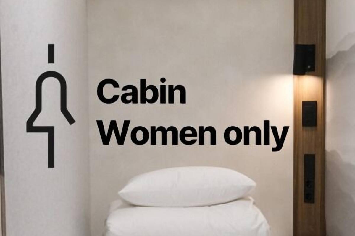 A cabin with a bed, a sign indicating it is for women only, and a wooden panel on the wall.