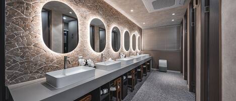 A modern bathroom with a stone wall, multiple sinks, and illuminated mirrors.