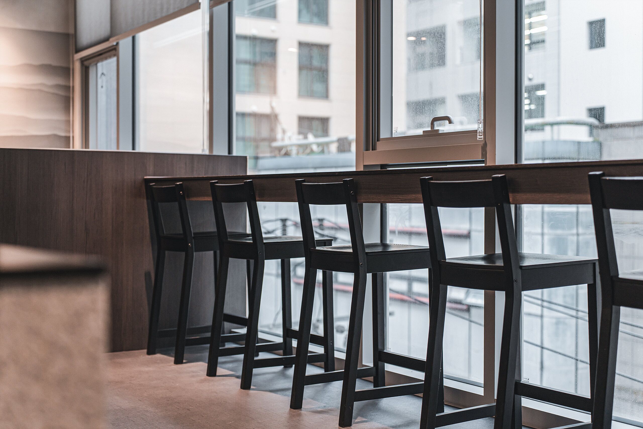 A row of wooden chairs and tables in a modern interior with large windows.