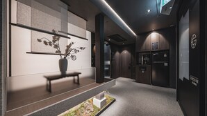 Een moderne lobby met een receptiebalie, een potplant, een kleine binnentuin en een receptiegedeelte met een counter en een bord.