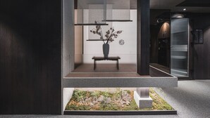 Een moderne lobby met een minimalistisch design, voorzien van een bank, een vaas met gedroogde bloemen en een kleine binnentuin.