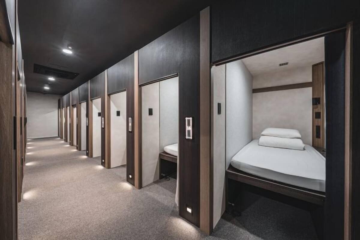 A hotel corridor with individual rooms featuring beds, toilets, and a carpeted floor.