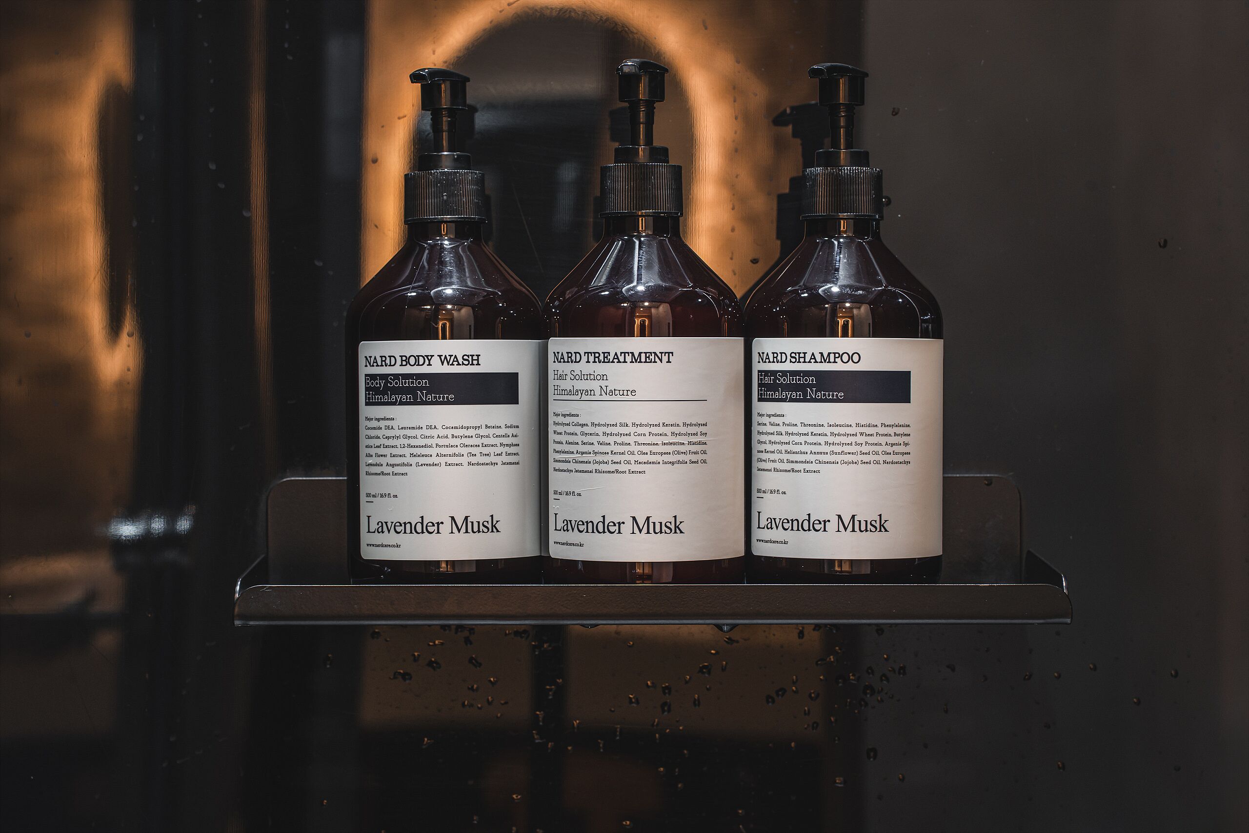 Three bottles of Nard Body Wash, Nard Treatment, and Nard Shampoo on a metal shelf.