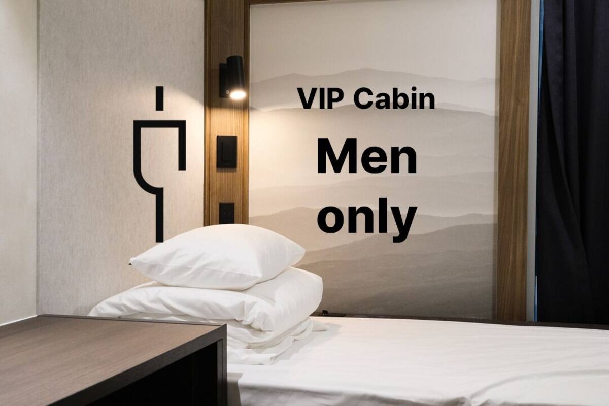 A room with a bed, a nightstand, and a wall-mounted light fixture. Text on the wall reads "VIP Cabin Men only".