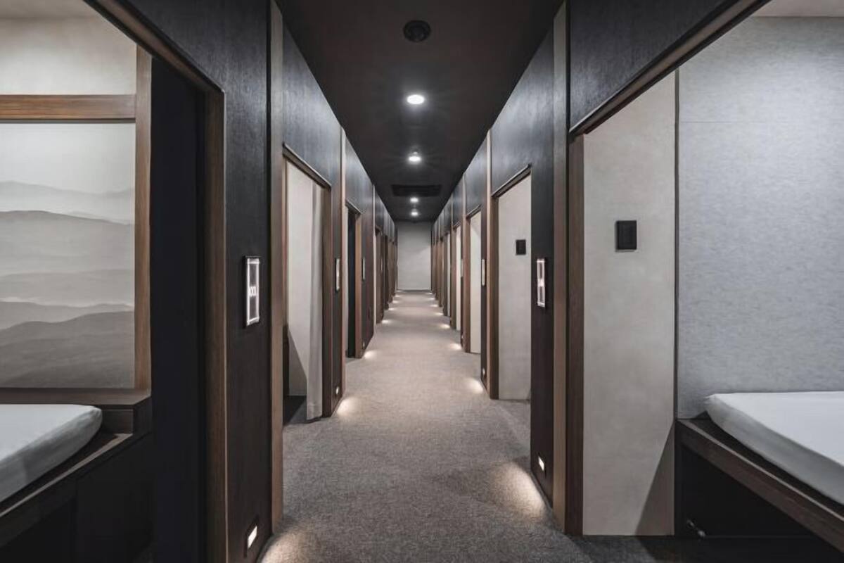 A hotel corridor with individual rooms, each with a bed and a door.