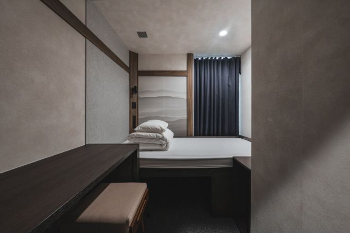 A compact hotel room with a bed, a small bench, and a window with curtains.
