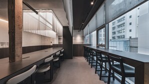 Een modern interieur met een lange tafel en stoelen, grote ramen en een uitzicht op een gebouw.