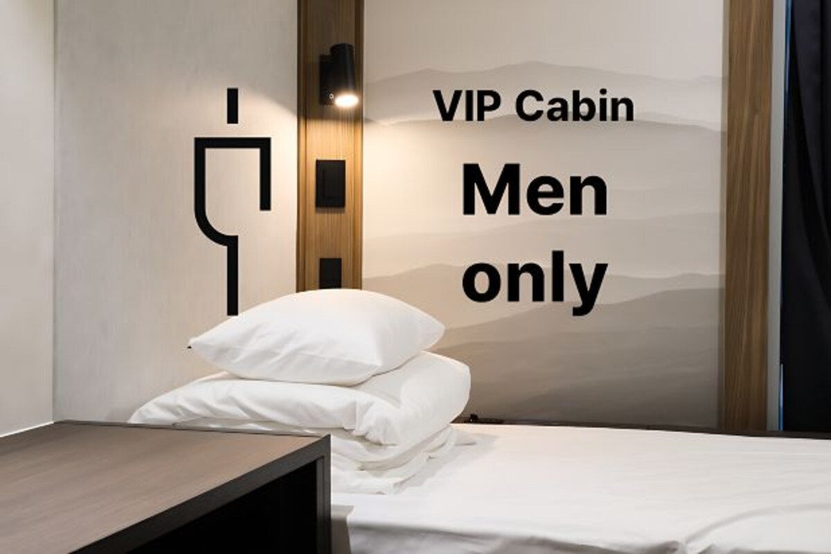 A room with a bed, a nightstand, and a wall with a sign reading "VIP Cabin Men only".
