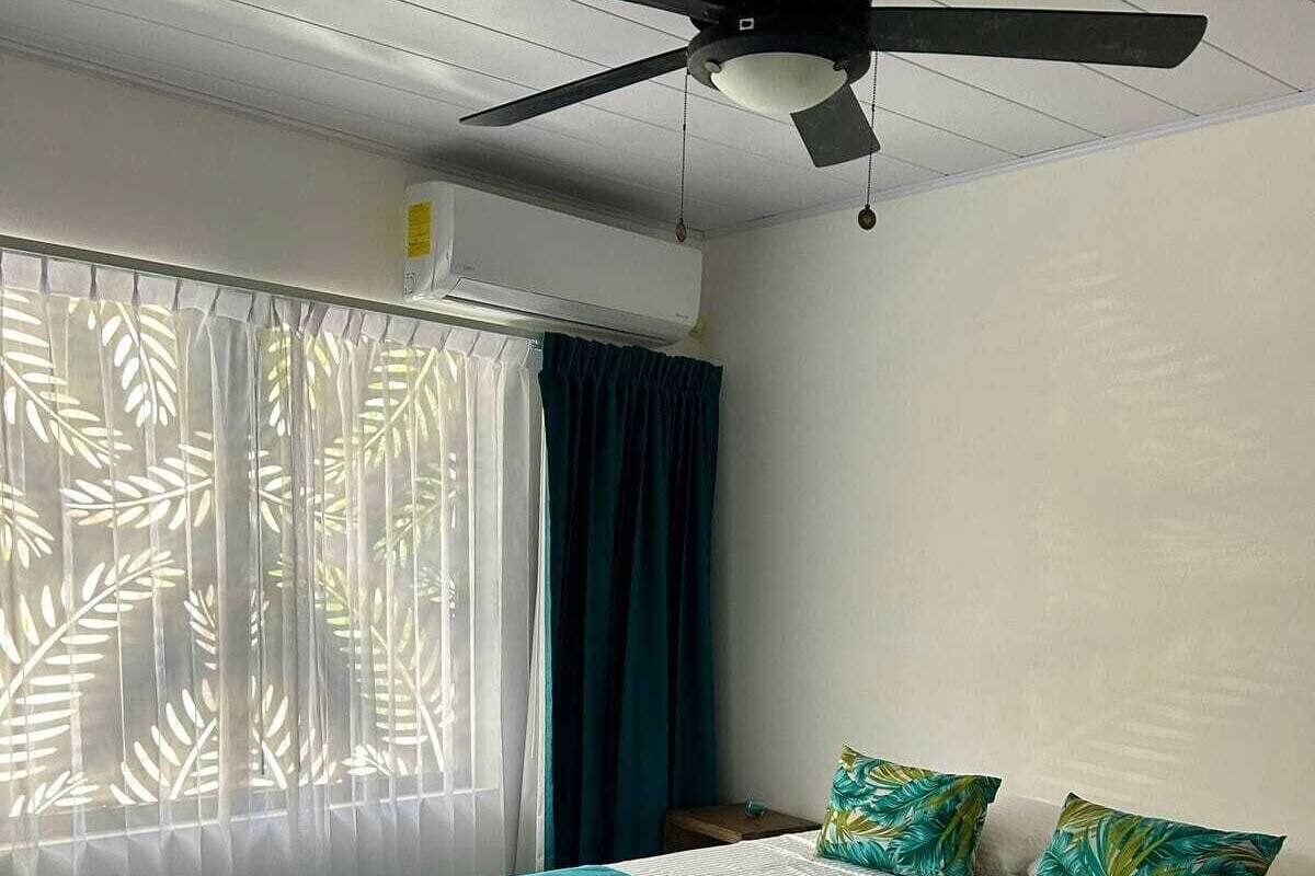 Un dormitorio con cama, cortinas, ventilador de techo y ventana con diseño de hojas.