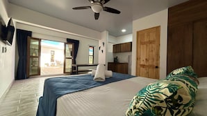 Une chambre d’hôtel avec un lit, un ventilateur de plafond, une vue sur la terrasse extérieure et une porte en bois.