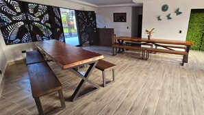 Un espace repas avec une longue table en bois et des bancs, un mur végétal et une plante en pot.