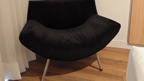 A black chair with metal legs in a room with wooden flooring and white curtains. - Flat 109 norte novo e completo (Brasilia)